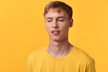 Sarı tişörtlü sıradan bir erkek model, sarı duvara dayanır, rahat ifade ve sıcak tonlar markalaşma, yaşam tarzı ve moda kampanyaları için idealdir..