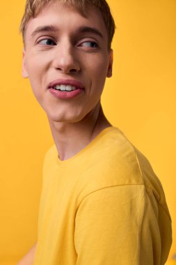 Sarı tişörtlü, canlı arka plan, rahat duruş, neşeli ruh hali ve moda ya da editoryal kullanım için modern yaşam tarzı olan genç bir adamın parlak stüdyo görüntüsü