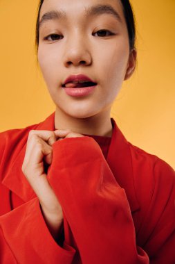 Closeup of female model in red outerwear holding collar with hand for fashion shoot. Clean skin, natural look and warm colored backdrop for stylish clothing advertisement.