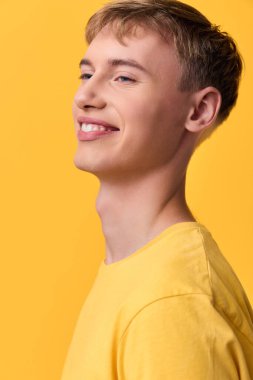 Cesur bir stüdyo ortamında sarı tişört giyen mutlu bir adam neşeli ışıklandırma ve basit bir gardırop hareketli, çağdaş bir yaşam tarzını ifade eder.