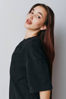 Portrait of young female with straight dark hair in casual black shirt posing near white wall with relaxed posture and subtle facial expression for fashion or lifestyle concept.