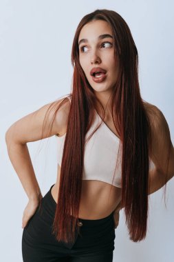 Uzun kahverengi saçlı, rahat giyimli, kalçasında elleri olan ve beyaz arka planda yana bakan çekici bir kadın modeli..