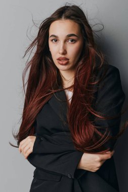 Siyah ceketli, kendine güvenen genç bir kadının portresi. Kolları gri duvarın yanında duruyor. Doğal güzelliği ve gündelik tarzını gösteriyor..