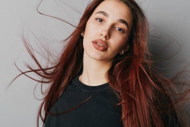 Siyah bluz giyen, kırmızı saçlı ve minimum makyajlı genç bir kadının portresi. Yumuşak ışıklandırma, gevşek saç hareketi ve güzellik konsepti için nötr gri arkaplan ile stüdyo fotoğrafı.