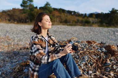 Kayalık bir sahilde fotoğraf makinesi, günlük giysiler içinde bir kamera, açık hava sahnesi plajı, kayaları, doğayı ve sükuneti vurgulayan yaratıcı keşiflerin ve sahil atmosferinin rahat bir anı.