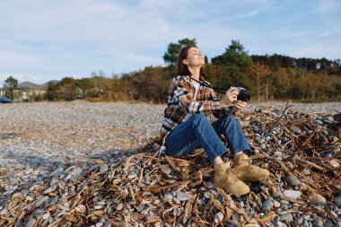 Deniz kabuğu sahilinde sıradan bir fotoğrafçı, çizme ve kareli gömlek giyerek, açık hava manzarasını ve sonbahar renklerini keşfederek doğada samimi bir anı yakalar.