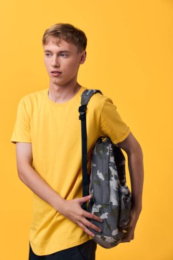 Sırt çantası ve rahat duruşu olan günlük öğrenci tarzı, canlı sarı bir sahnede şehir modası, sınıf veya seyahat için hazır, canlı renk ve günlük taşıma