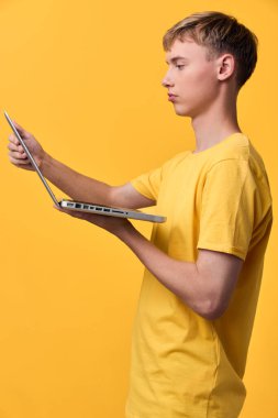 Stüdyoda dizüstü bilgisayarı olan odaklanmış genç bir adam, dijital yaşam tarzı mesajlaşması için canlı turuncu bir arka plana karşı teknoloji kullanımı, çalışma ve verimliliği vurguluyor.