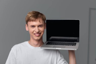 Sıradan teknoloji sahnesi, basit bir stüdyo ortamında, erişilebilir dijital araçları, dostane titreşimleri ve çağdaş iş akışını vurgulayan bir adamın dizüstü bilgisayar sunuşunu gösteriyor..