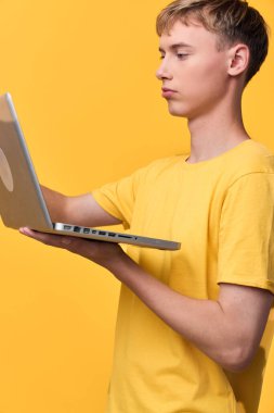 Bilgisayarlı genç adam teknolojiyi keşfediyor ve canlı sarı bir zemin üzerinde öğreniyor. Konsantrasyon, online çalışma ve dijital cihazların yaratıcı kullanımı üzerinde çalışıyor.