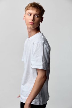 Casual style in studio scene features a young man in a white T shirt, side gaze, minimal background, clean composition, versatile fashion or lifestyle stock photo.