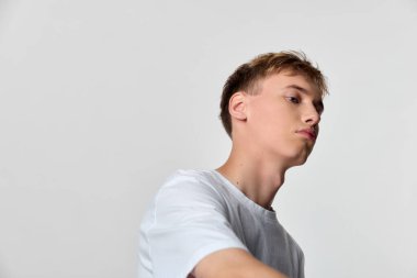 Temiz, nötr bir zemin üzerine kurulmuş beyaz tişört giyen genç bir adamın açılı profili, sakin tavırları, basit gardırobu ve stok fotoğrafçılığı ve moda için uygun modern minimalizmi vurguluyor.