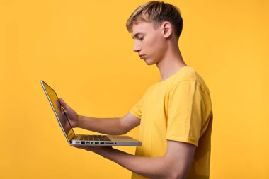 Gündelik stüdyo sahnesi, dokunmatik ekran etkileşimini, yeniliği, eğitimi ve tek renkli sarı ayar ve temiz modern atmosfer içerisindeki uzaktan çalışmayı vurgulayan bir dizüstü bilgisayar kullanan odaklanmış bir genci gösteriyor.