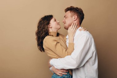 Sevecen genç bir çift birbirine sarılıyor bej kazaklı bir kadın ve beyaz gömlekli bir adam birbirlerine bakıyor. Sade arka planda romantik bir an. İlişki ve şefkat kavramı.