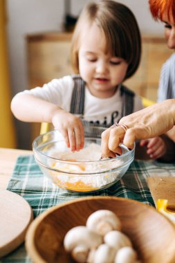 Evde birlikte yemek pişirin. Kızıl saçlı büyükanne ve küçük torun rahat bir evde pizza pişiriyorlar. Mutfakta iyi eğlenceler.