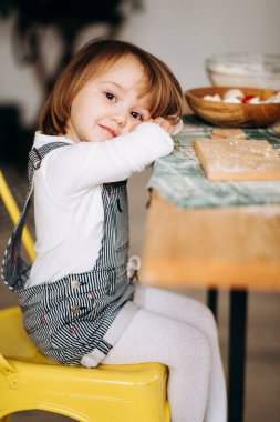 Küçük güzel sarışın kız mutfakta oynuyor. Masada malzemeleri gösterir