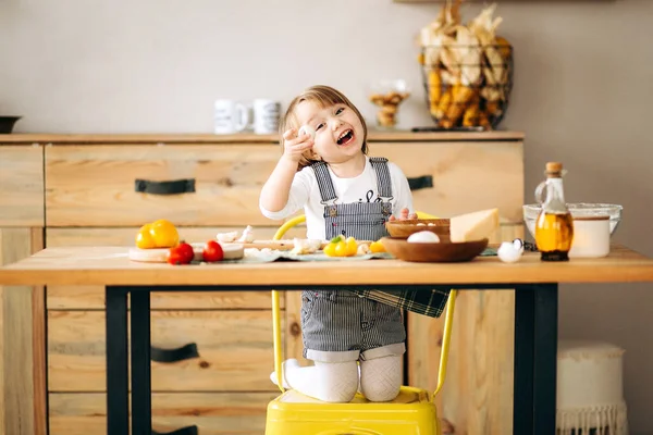 Little beautiful blonde girl playing in the kitchen. Shows ingredients on the table