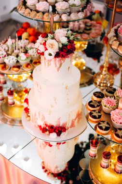 Pasta, kurabiye, tatlı ve yuvarlak bir masada çiçeklerle süslenmiş meyveli çikolata.