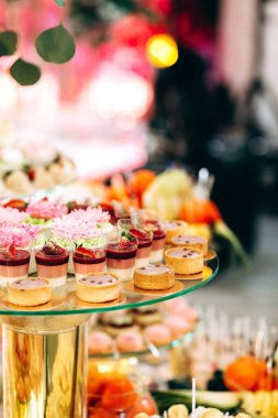 Pasta, kurabiye, tatlı ve yuvarlak bir masada çiçeklerle süslenmiş meyveli çikolata.