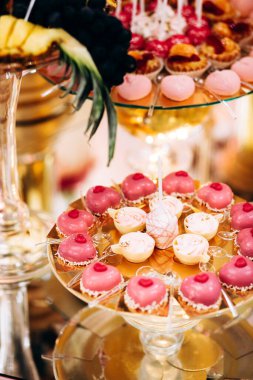 Pasta, kurabiye, tatlı ve yuvarlak bir masada çiçeklerle süslenmiş meyveli çikolata.