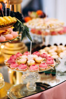 Pasta, kurabiye, tatlı ve yuvarlak bir masada çiçeklerle süslenmiş meyveli çikolata.