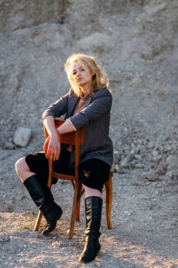 Gün batımında kumlu bir kanyonda eski bir sandalyede oturan kızıl saçlı kız. Yalnızlığın psikolojik portresi. Hipster eski moda konsepti