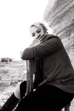 Gün batımında kumlu bir kanyonda eski bir sandalyeyle poz veren kızıl saçlı kız. Yalnızlığın psikolojik portresi. Hipster eski moda konsepti