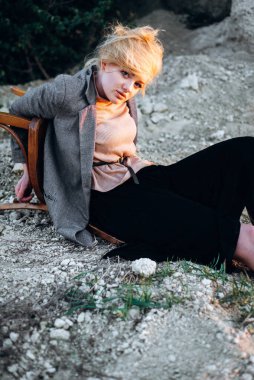 Gün batımında kumlu bir kanyonda eski bir sandalyeyle poz veren kızıl saçlı kız. Yalnızlığın psikolojik portresi. Hipster eski moda konsepti