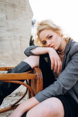 Gün batımında kumlu bir kanyonda eski bir sandalyeyle poz veren kızıl saçlı kız. Yalnızlığın psikolojik portresi. Hipster eski moda konsepti