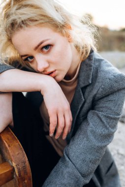 Gün batımında kumlu bir kanyonda eski bir sandalyeyle poz veren kızıl saçlı kız. Yalnızlığın psikolojik portresi. Hipster eski moda konsepti