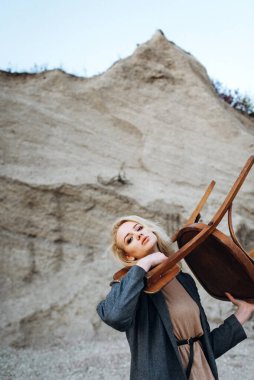 Gün batımında kumlu bir kanyonda eski bir sandalyeyle poz veren kızıl saçlı kız. Yalnızlığın psikolojik portresi. Hipster eski moda konsepti