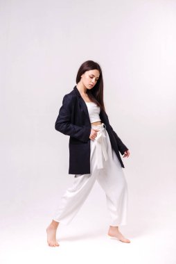 Beyaz eko pantolonlu güzel bir esmerin moda portresi ve beyaz arka planda koyu renk bir ceket. Eko giyim konsepti