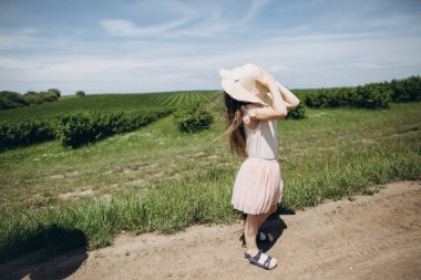 Yazın yeşil bir arazide şapkalı küçük bir kız yürüyor. Arka görünüm