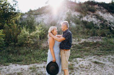 Kayaların arasındaki parkta kucaklaşan mutlu kıdemli adam ve kadın. Kıdemli çift yazın yürüyor ve eğleniyor.