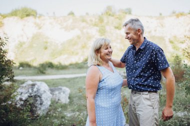 Kayaların arasındaki parkta kucaklaşan mutlu kıdemli adam ve kadın. Kıdemli çift yazın yürüyor ve eğleniyor.