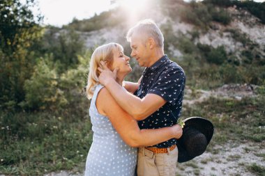 Kayaların arasındaki parkta kucaklaşan mutlu kıdemli adam ve kadın. Kıdemli çift yazın yürüyor ve eğleniyor.