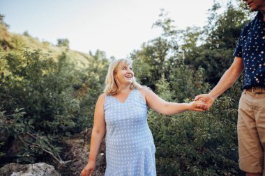 Yaşlı çift doğada dinleniyor ve el ele tutuşuyorlar.