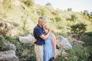 Kayaların arasındaki parkta kucaklaşan mutlu kıdemli adam ve kadın. Kıdemli çift yazın yürüyor ve eğleniyor.