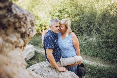 Kayaların arasındaki parkta kucaklaşan mutlu kıdemli adam ve kadın. Kıdemli çift yazın yürüyor ve eğleniyor.
