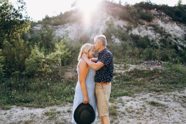 Kayaların arasındaki parkta kucaklaşan mutlu kıdemli adam ve kadın. Kıdemli çift yazın yürüyor ve eğleniyor.