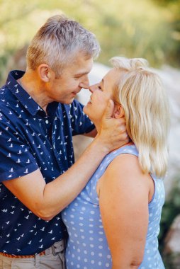 Kayaların arasındaki parkta kucaklaşan mutlu kıdemli adam ve kadın. Kıdemli çift yazın yürüyor ve eğleniyor.