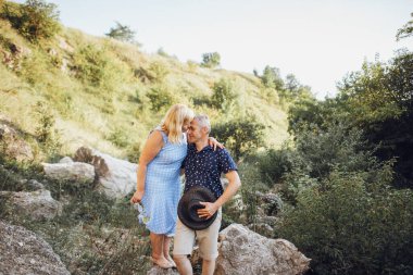 Kayaların arasındaki parkta kucaklaşan mutlu kıdemli adam ve kadın. Kıdemli çift yazın yürüyor ve eğleniyor.