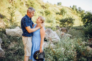 Kayaların arasındaki parkta kucaklaşan mutlu kıdemli adam ve kadın. Kıdemli çift yazın yürüyor ve eğleniyor.