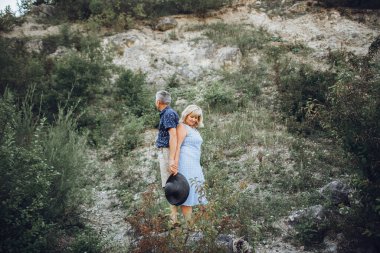Yaşlı çift doğada dinleniyor ve el ele tutuşuyorlar.