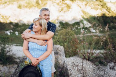 Kayaların arasındaki parkta kucaklaşan mutlu kıdemli adam ve kadın. Kıdemli çift yazın yürüyor ve eğleniyor.