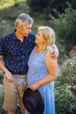 Kayaların arasındaki parkta kucaklaşan mutlu kıdemli adam ve kadın. Kıdemli çift yazın yürüyor ve eğleniyor.