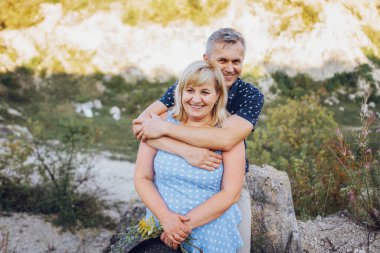 Kayaların arasındaki parkta kucaklaşan mutlu kıdemli adam ve kadın. Kıdemli çift yazın yürüyor ve eğleniyor.