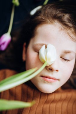 Kız karanlık bir arka planda lalelerin içinde yatıyor. Anneler Günün kutlu olsun.