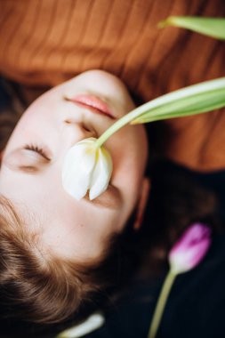 Kız karanlık bir arka planda lalelerin içinde yatıyor. Anneler Günün kutlu olsun.