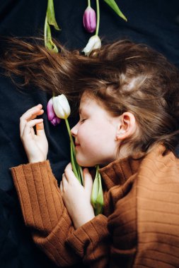 Kız karanlık bir arka planda lalelerin içinde yatıyor. Anneler Günün kutlu olsun.